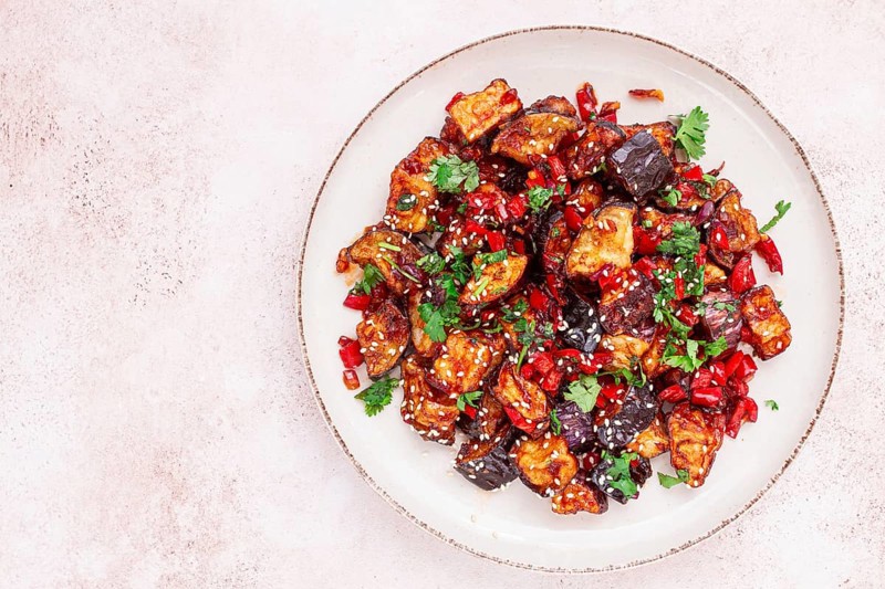 Fried eggplant, Chinese style, in sweet and sour sauce, with pepper and sesame seeds. on a white plate