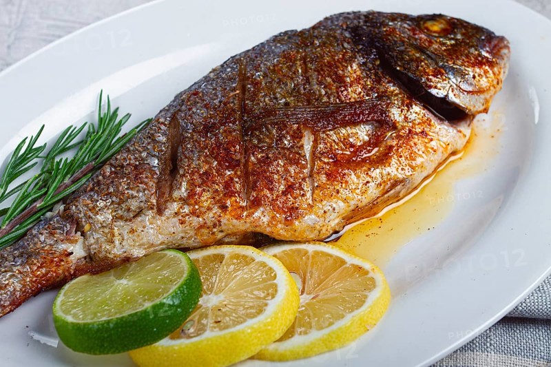 Baked dorado fish, in the oven, fried dorado, with spices and herbs, on a white plate, top view, homemade, no people