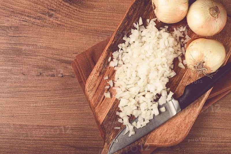 Finely chopped onion on a chopping board with a knife, wooden table, top view, no people