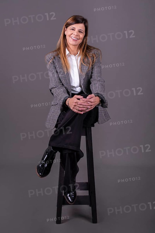 Elegant senior businesswoman sitting on a stool and smiling at the camera