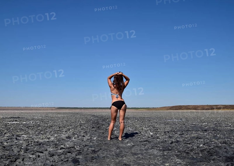 Walk the dark-haired woman in a swimsuit on the bottom of a dry lake with salt and mud. Taman, Krasnodar Krai, Russia