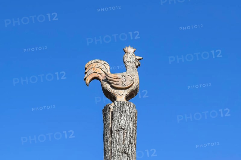 Figurine of a rooster on a tree stump on a background of blue sky. Taman, Krasnodar Krai, Russia