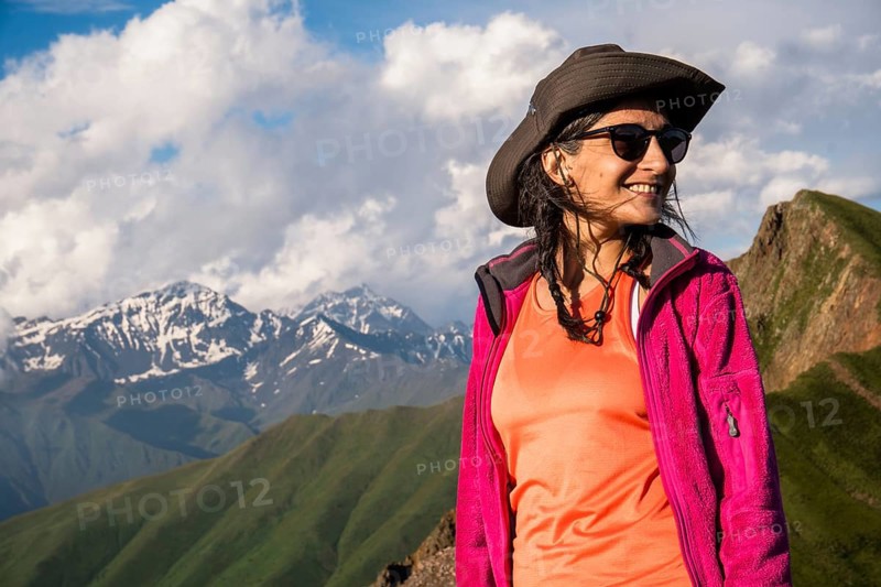 Happy Young Traveler hiker woman portrait wearing hat and jacket smiling in Kazbegi National Park mountains of Georgia, adventure lifestyle and hiking portrait