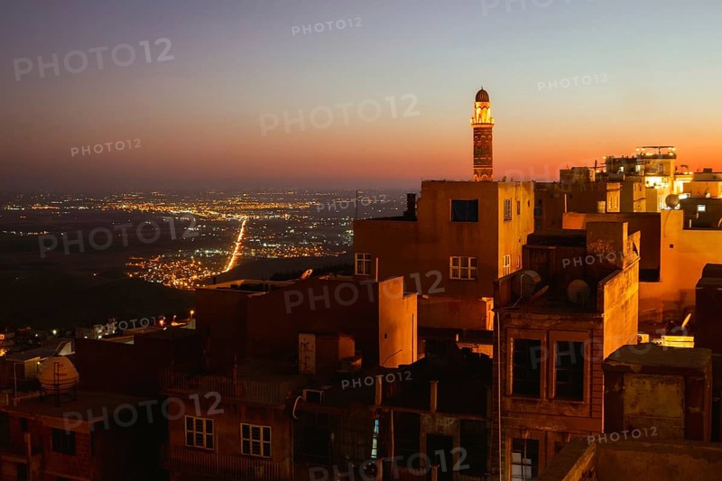 Illuminated mosque minaret above Mardin old town with glowing city lights and Mesopotamian plains at sunset. Great Mosque of Mardin Ulu Camii Minaret