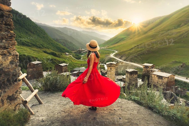 Woman in red dress looking at medieval towers of Ushguli Georgia during sunset with mountains and Enguri valley landscape