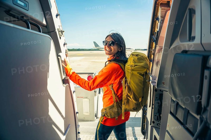 Young happy caucasian female traveler backpacker with carry on hiking backpack boarding airplane pose at aircraft entrance smiling, adventure tourism lifestyle, journey. Weekend trip get away Europe