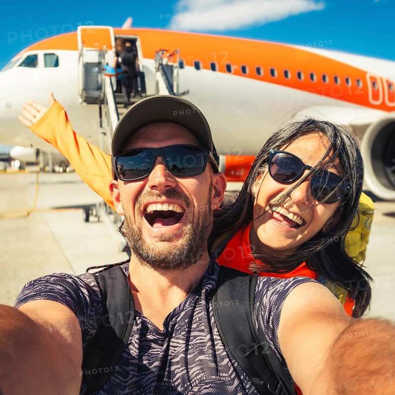 Happy couple of tourists boarding outside to plane at the airport - Happy man and woman having happy summer vacation together - Transportation and holidays