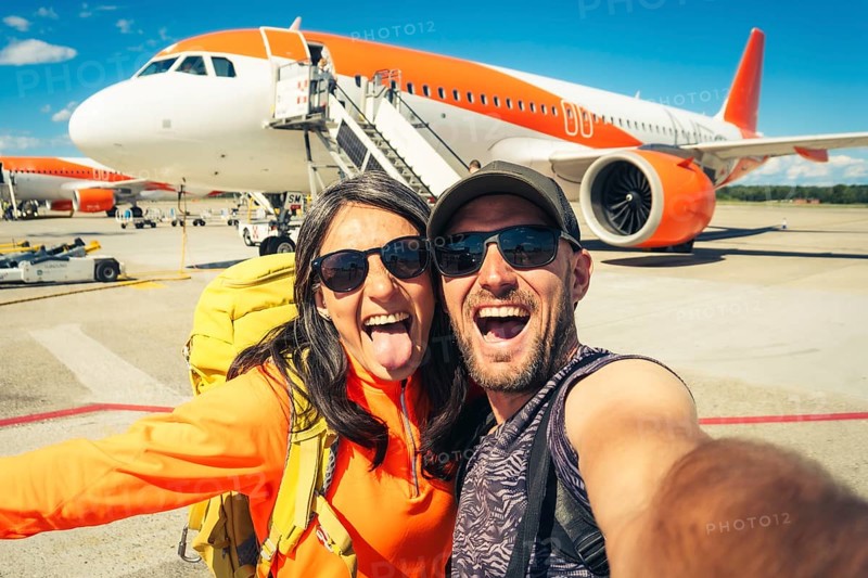 Young happy caucasian couple taking selfie portrait on departure or arrival destination for vacation on sunny autumn day. Budget student travelers, vacationist, explorers having fun. Weekend escape