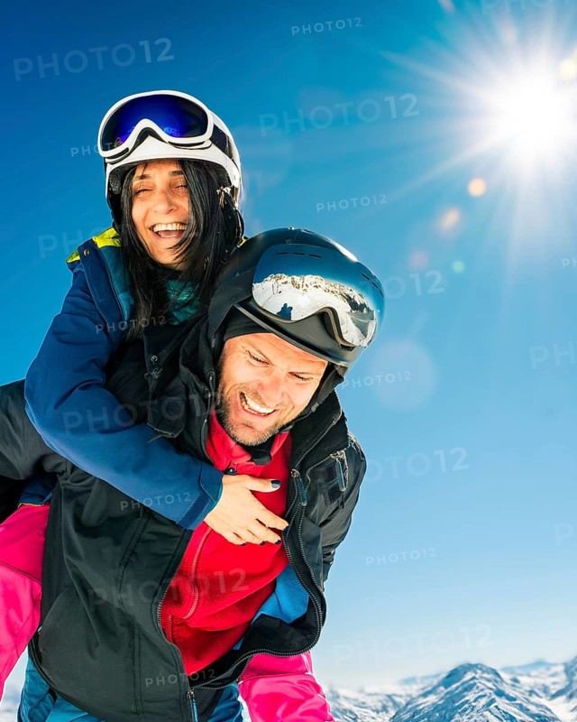 Romantic happy skiers couple in love having fun together playing in mountains piggybacking at wintertime.Winter lovers couple isolated mock up outdoors blue banner copy space background