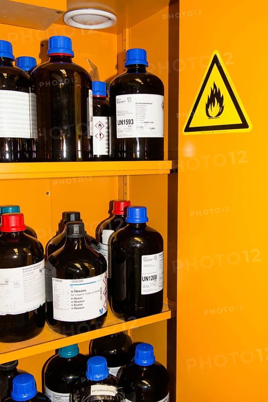 Flammable Chemicals In Bottles With Different Size in Orange Protection Cabinet, Marked With A Flammable Warning Sign