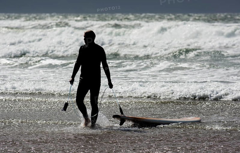 Silhouette Of A Surfer With His Surfboard Leaving Water Of Cold Atlantic At The Coast Of Ireland