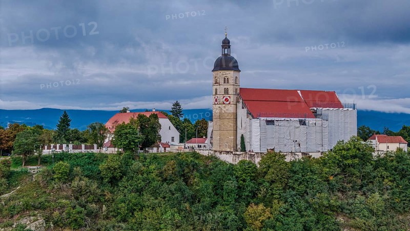 The pilgrimage church of the Assumption of the Virgin Mary on the Bogenberg is surrounded by scaffolding during its renovation. Gentle hills and a cloudy sky are visible in the background. Bogen, Lower Bavaria