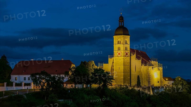 The pilgrimage church of the Assumption of the Virgin Mary on the Bogenberg has a golden light in the evening that emphasises its beauty. Surrounded by trees and buildings, it presents itself in a peaceful atmosphere. Bogen, Lower Bavaria