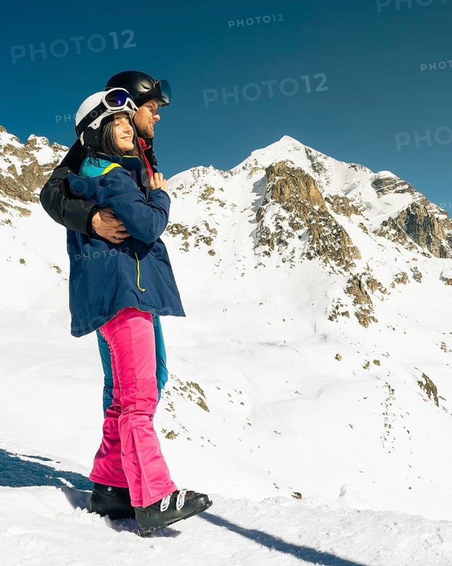 Young caucasian couple pose hug enjoying looking at snowy mountains range in winter. Get away skiing holidays lifestyle. Tetnuldi ski resort viewpoint. Caucasus mountains high altitude freeriding