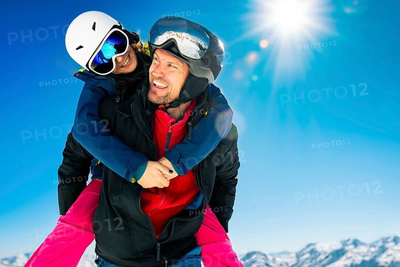 Romantic happy skiers couple in love having fun together playing in mountains piggybacking at wintertime.Winter lovers couple isolated mock up outdoors blue banner copy space background