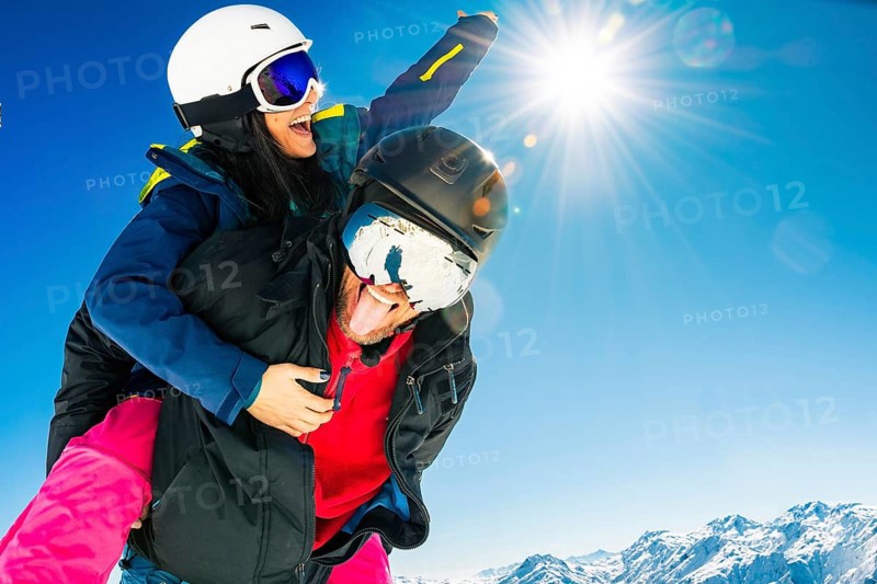 Romantic happy skiers couple in love having fun together playing in mountains piggybacking at wintertime.Winter lovers couple isolated mock up outdoors blue banner copy space background