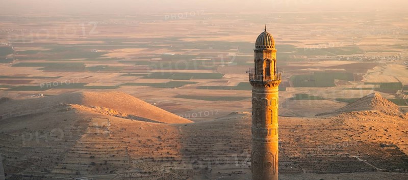 Historic Ulu Cami mosque minaret in Mardin Turkey illuminated by sunset against vast Mesopotamian plains and Anatolian landscape