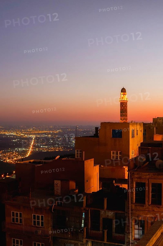 Illuminated mosque minaret above Mardin old town with glowing city lights and Mesopotamian plains at sunset. Great Mosque of Mardin Ulu Camii Minaret