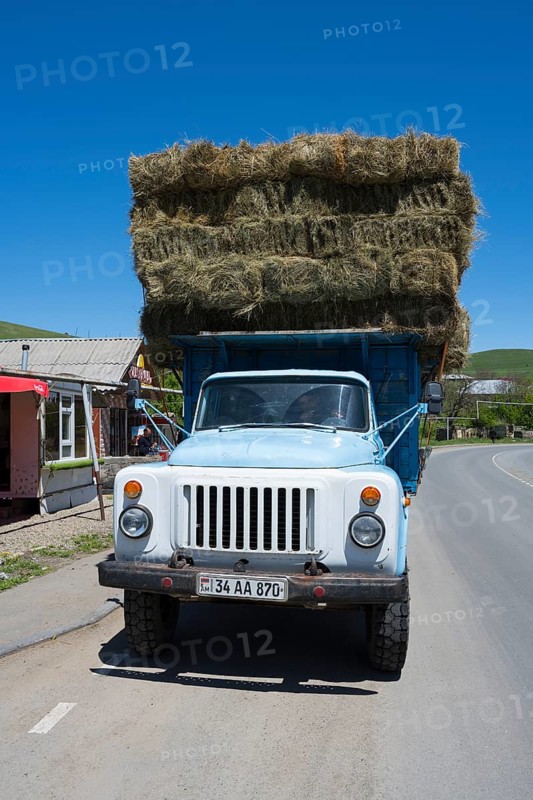 A blue lorry loaded with several layers of hay bales is parked on a country road, Armenia