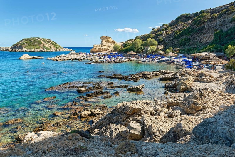 Grande Blue rocky beach with blue sea, umbrellas and surrounding cliffs under clear skies, Grande Blue Beach, Stegna, Archangelos, Rhodes Island, Greece