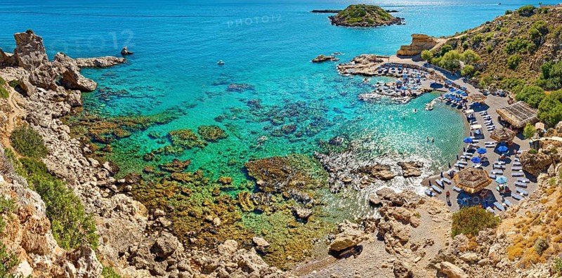Secluded Grande Blue Bay with clear turquoise water and rocks, along which a row of beach loungers and parasols stretches, Grande Blue Beach, Stegna, Archangelos, Rhodes Island, Greece