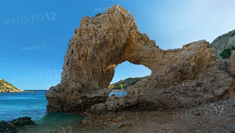 Rock arch at Grande Blue Beach under a clear blue sky in a sunny coastal landscape, Grande Blue Beach, Stegna, Archangelos, Rhodes Island, Greece