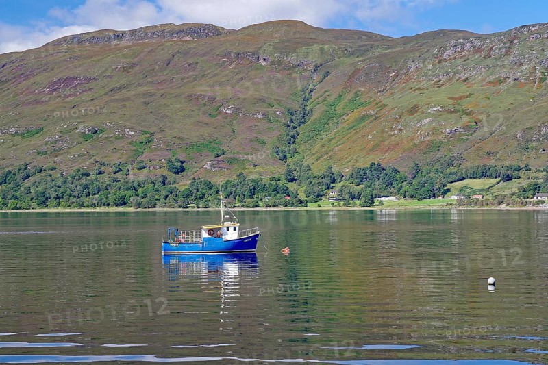 Small boat floating on a calm lake surrounded by green mountains, Fort William, Scotland, United Kingdom