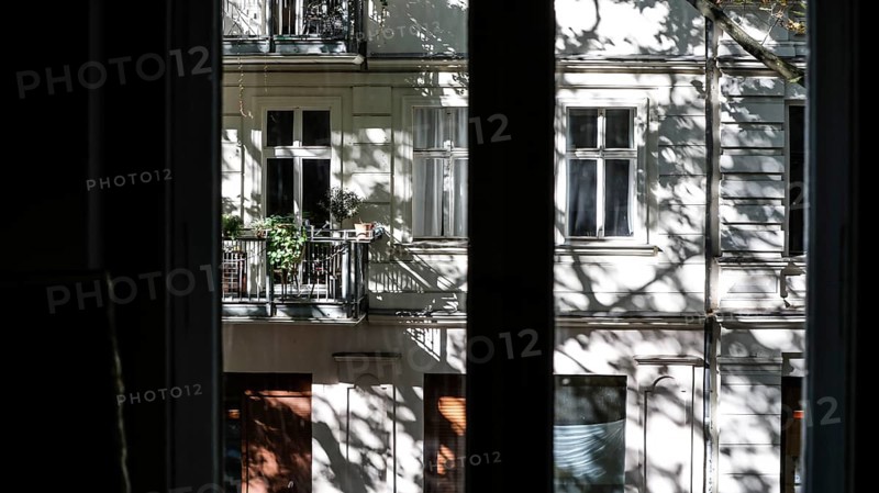 View through a window to an opposite facade of a multi-storey residential building with classical architecture and balconies with plants, shadows of leaves and branches on the house wall, Berlin, 24.09.2025, Berlin, Berlin, Germany