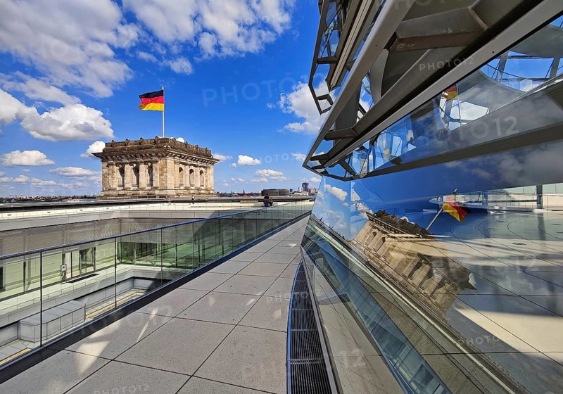 Viewing platform with a German flag in the wind on one of the corner towers and reflection in the Reichstag dome, government district, Berlin, Germany