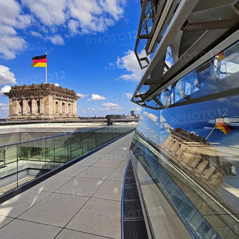 Viewing platform with a German flag in the wind on one of the corner towers and reflection in the Reichstag dome, government district, Berlin, Germany