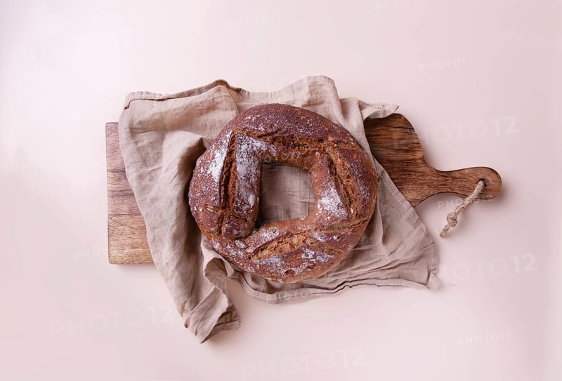 Round handmade rye bread on wooden board with linen napkin, on beige background top view, copy space