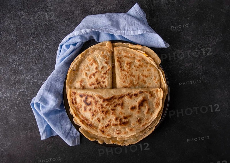 Appetizing pancakes with filling on a plate with a blue napkin, on a black background, space for text, top view