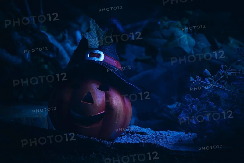Blue illuminated pumpkin lantern with witch's hat on a dark night