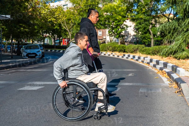 Two diverse young individuals with disabilities walking on a city road, one person using a wheelchair and the other a prosthetic leg, embodying urban mobility, inclusion, and friendship
