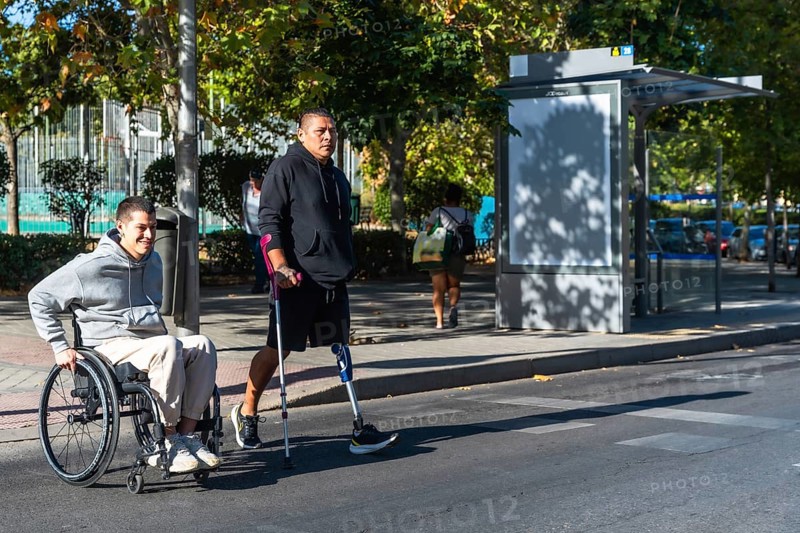 Two amputee men, one using a wheelchair and the other a prosthetic leg with crutch, navigating an urban environment, symbolizing friendship, support, and active movement