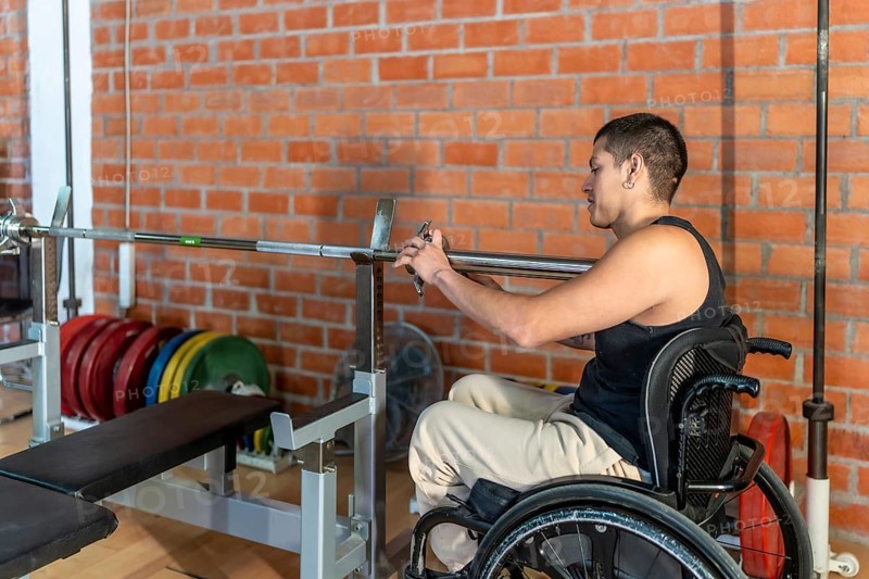 Young man in a wheelchair setting up a barbell in a modern gym, focused and determined as he trains for strength, adaptive fitness and rehabilitation progress