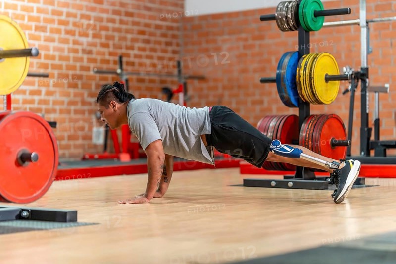 Athlete with a prosthetic leg doing push ups on a gym floor, showing determination, adaptive fitness and strength during rehabilitation and focused training session