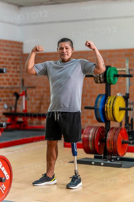 Amputee man with a prosthetic leg standing confidently in a gym, flexing his biceps and looking at camera, symbolizing strength, resilience and recovery through fitness rehabilitation