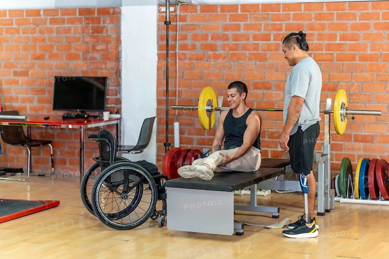 Two adaptive athletesone with a prosthetic leg and one using a wheelchairsupport each other during gym training, showcasing inclusion, teamwork, and active recovery
