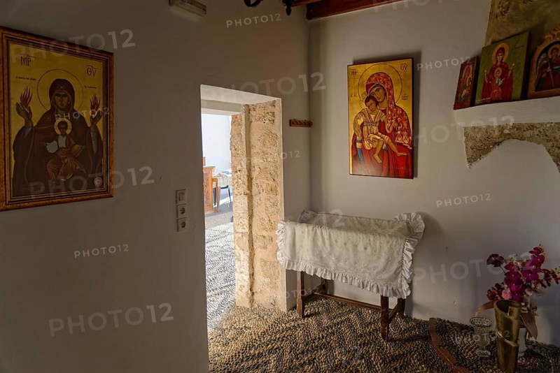 Room with religious icons of the Church of the Virgin Mary Tsambika (Kyra Psili), in warm lighting, including a white covered chest and a touch of natural light, Church of the Virgin Mary Tsambika (Kyra Psili), Archangelos, Rhodes Island, Greece