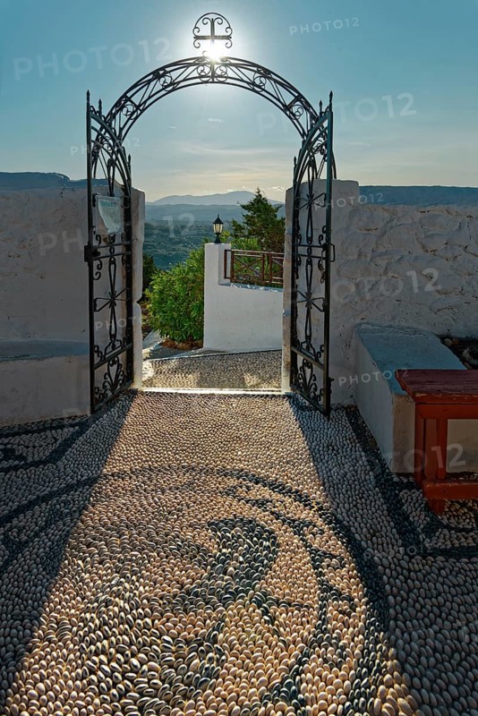Open Tor tor of the Church of the Virgin Mary with ornate pebble paving and view of sunny Mediterranean landscape, Church of the Virgin Mary Tsambika (Kyra Psili), Archangelos, Rhodes Island, Greece