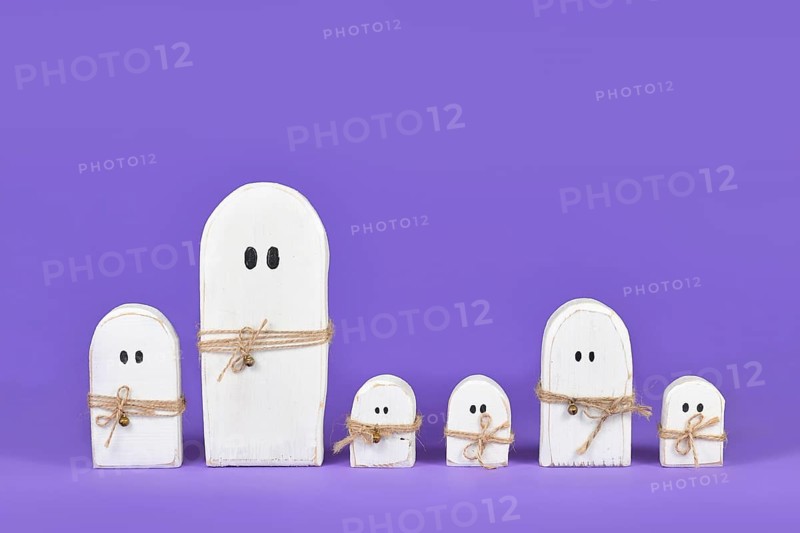 Cute wooden white Halloween ghost ornaments in a row on purple background