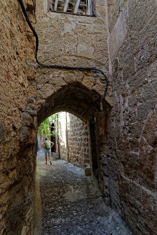 Cobbled alley with arched passageway and stone walls, a man in the background, Medieval town of Rhodes, Rhodes Island, Greece