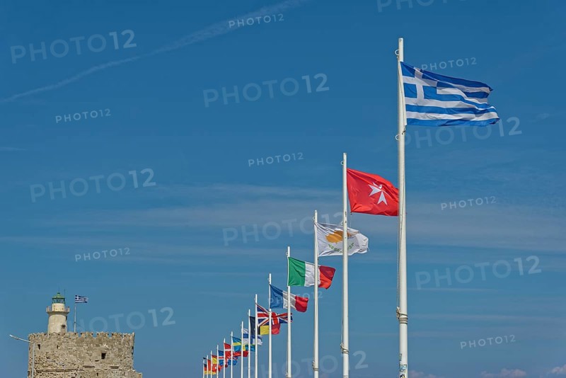 Several flags waving in the wind against a clear blue sky, including the Greek flag, Mandraki Harbour, Medieval Town of Rhodes, Rhodes Island, Greece