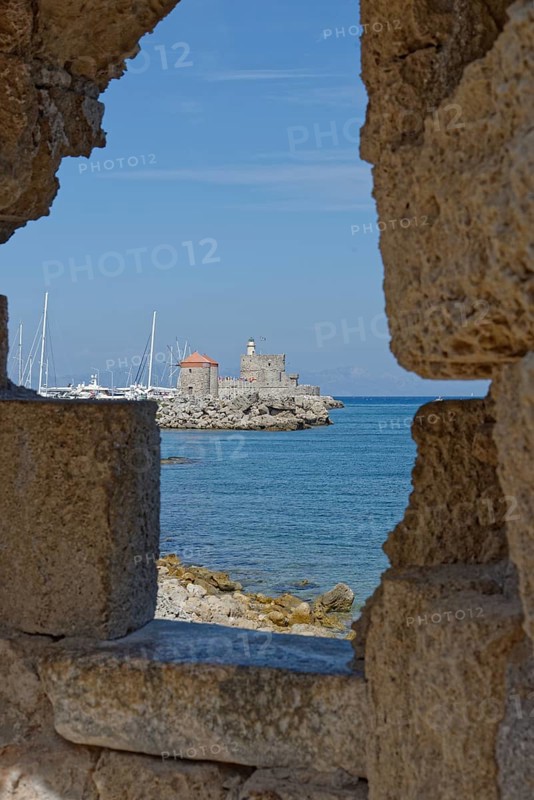 View through a wall of a medieval fort of Saint Nikolaos by the sea with sailing boats, Mandraki harbour, Medieval town of Rhodes, Rhodes island, Greece