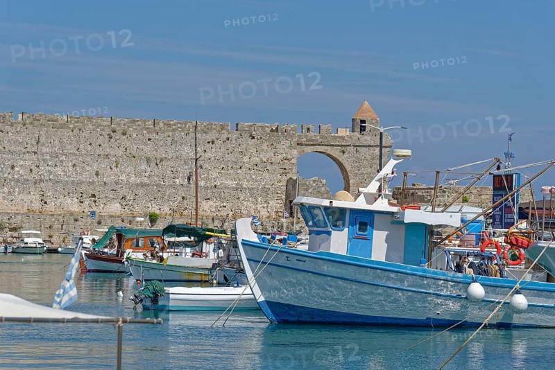 Fishing boats lying in the calm water in front of a historic city wall, Mandraki harbour, Medieval town of Rhodes, Rhodes island, Greece
