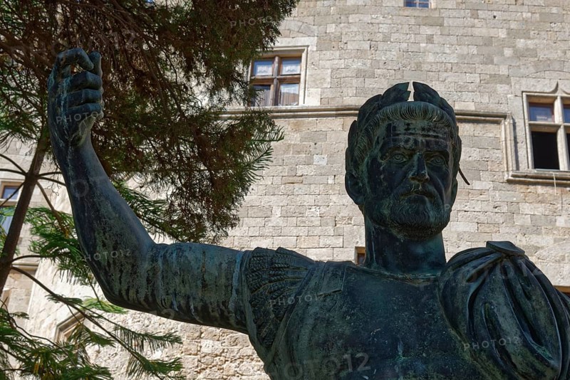 Statue of a man in ancient armour in front of a stone building with windows and trees, Grand Master's Palace, Medieval Town of Rhodes, Rhodes Island, Greece