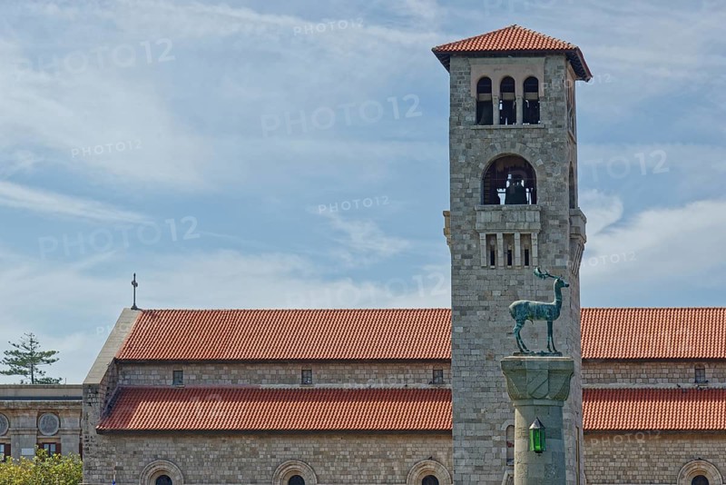 A church Ekklisia Evaggelismos with red roof and bell tower, in the foreground the deer cow statue (Colossus of Rhodes), Mandraki harbour, Medieval town of Rhodes, Rhodes island, Greece