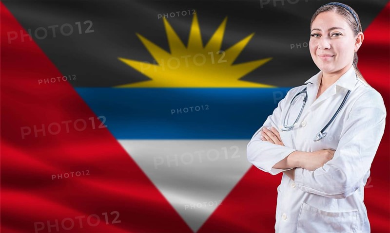 Female doctor on Antigua and Barbuda flag. Doctor with crossed arms on Antigua and Barbuda flag. Antigua and Barbuda health and care concept