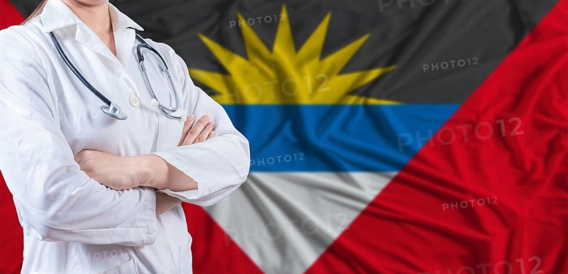 Doctor with crossed arms on Antigua and Barbuda flag. Antigua and Barbuda health and care concept. Female doctor on Antigua and Barbuda flag